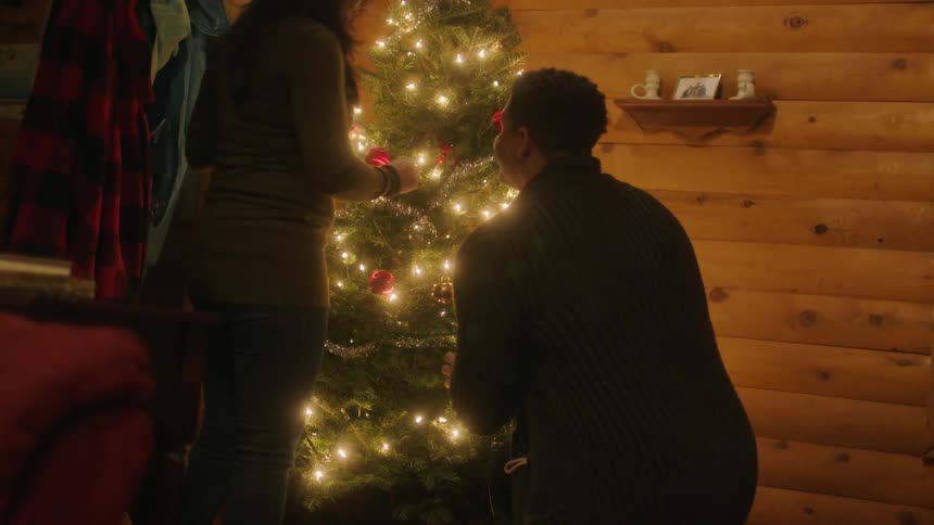 A man and woman decorate a christmas tree