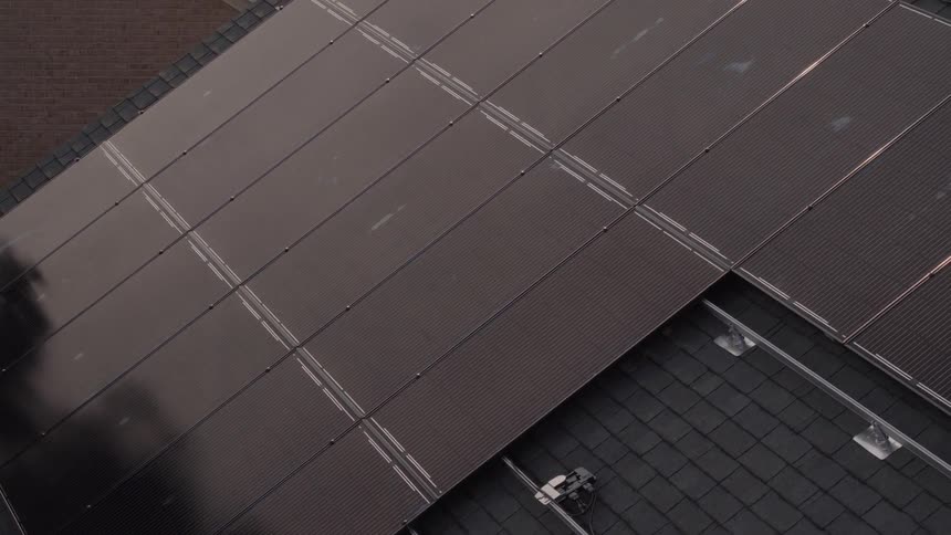 A man carrying a solar panel climbs a ladder to the roof