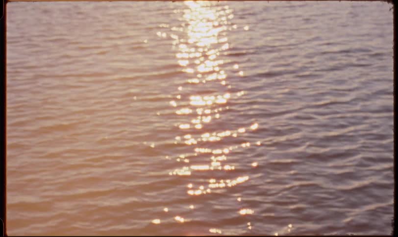 Golden sunlight glitters and reflects on the rippling water's surface, slowly transitioning into a soft, beautiful bokeh