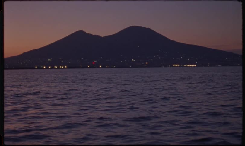 A vintage film captures the serene silhouette of Mount Vesuvius over the Bay of Naples at twilight