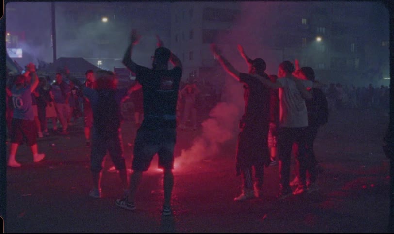 Vintage-style footage shows sports fans celebrating in the street at night around a red flare