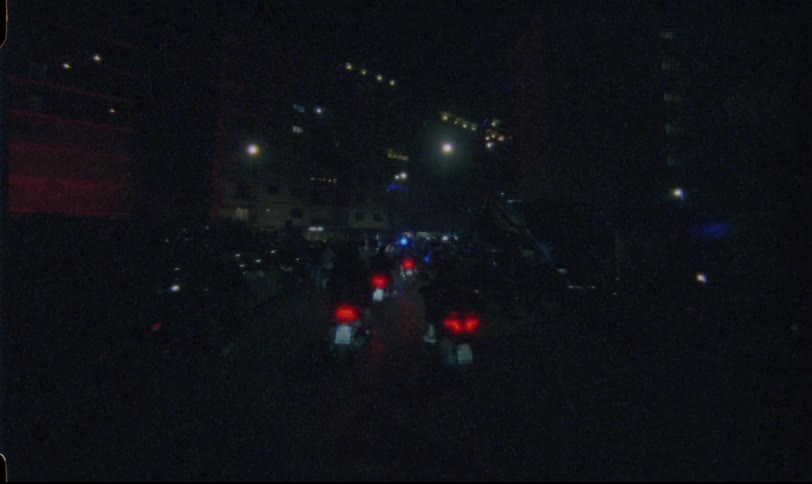 Vintage film footage captures a massive procession of motorcyclists taking over a city street at night during a rally