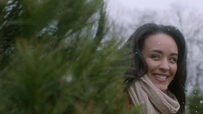 Woman looks beyond a tree smiling on a snowy day