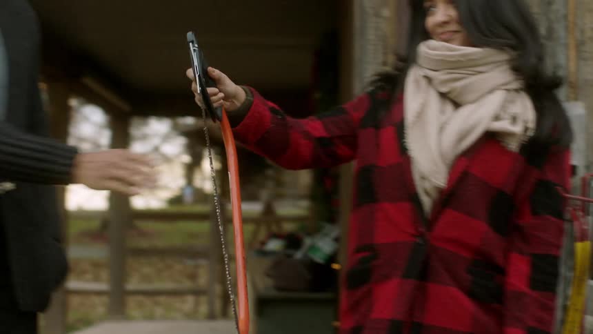 A man and woman pick up a handsaw outside a cabin