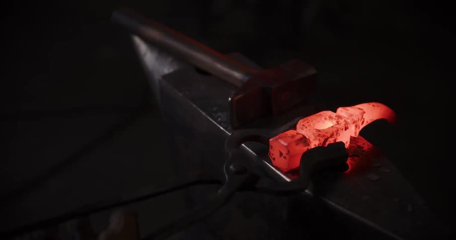 A blacksmith forges a glowing piece of red-hot metal on an anvil with a hammer in a dark workshop