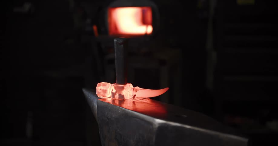 A blacksmith pulls a glowing hot piece of steel from the furnace and uses a hammer and anvil to forge it into shape