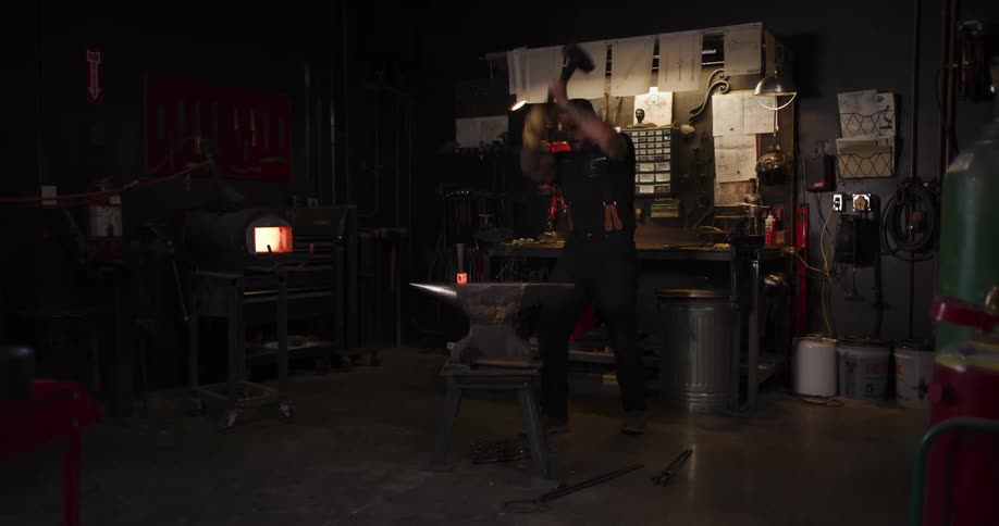 A tattooed blacksmith intensely hammers a glowing piece of metal on an anvil in his dimly lit forge