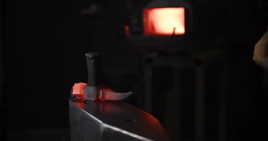 A blacksmith hammers a glowing piece of red-hot metal on an anvil in a dark workshop with a forge in the background