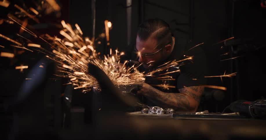 A skilled metalworker in a dark workshop uses an angle grinder, sending a brilliant shower of sparks flying in slow motion