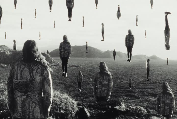 Surreal black and white landscape where multiple versions of the same person float mysteriously over a barren field