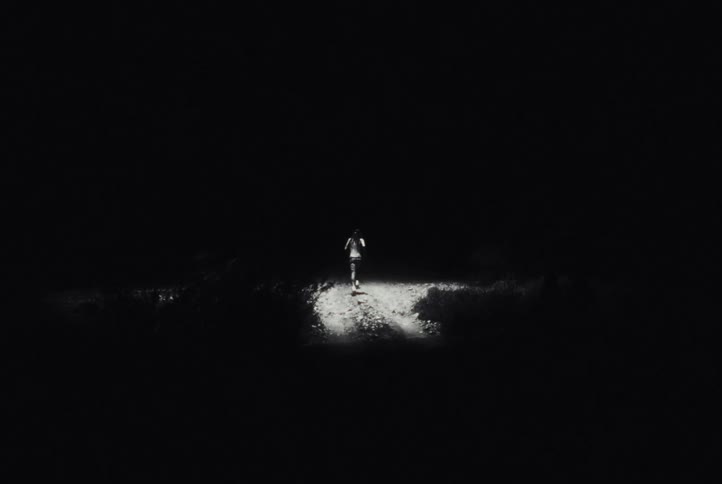 An experimental black and white clip shows a figure running down a dark path at night, intercut with an extreme close-up of a wide, intense eye