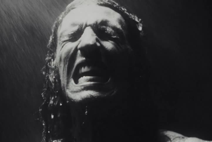 Intense black and white slow-motion footage shows a man screaming in anguish as rain pours down on his face