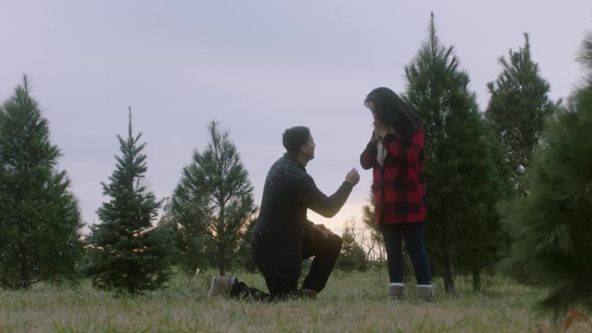 Man bends down on one knee to propose to woman outdoor while it snows