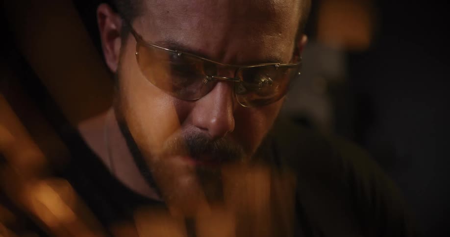A focused craftsman in safety glasses is illuminated by a shower of sparks from his grinder in a dark workshop