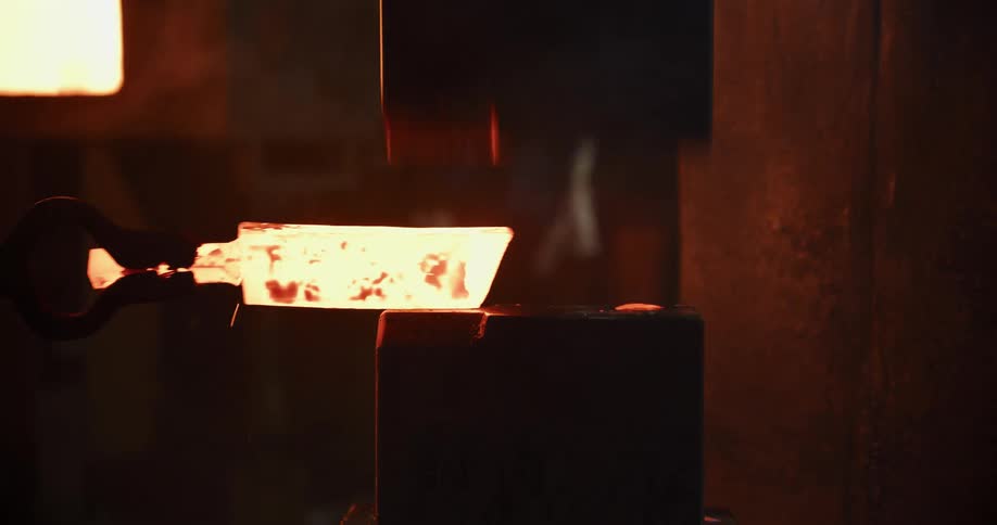 A powerful hydraulic press forges a glowing hot piece of metal, sending flames and sparks flying in a dark workshop