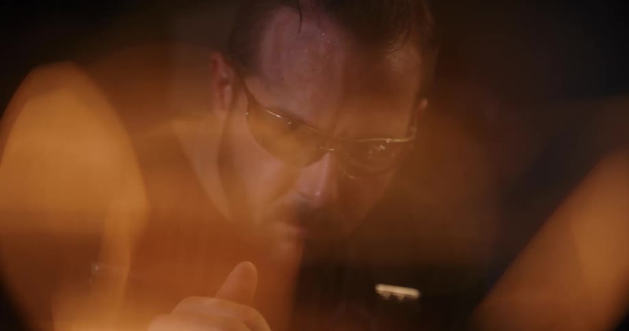 Close-up of a focused craftsman working in a dark workshop, with warm, fiery bokeh in the foreground