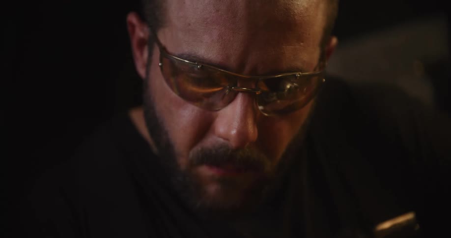 A close-up of a bearded craftsman with safety glasses concentrating on his work