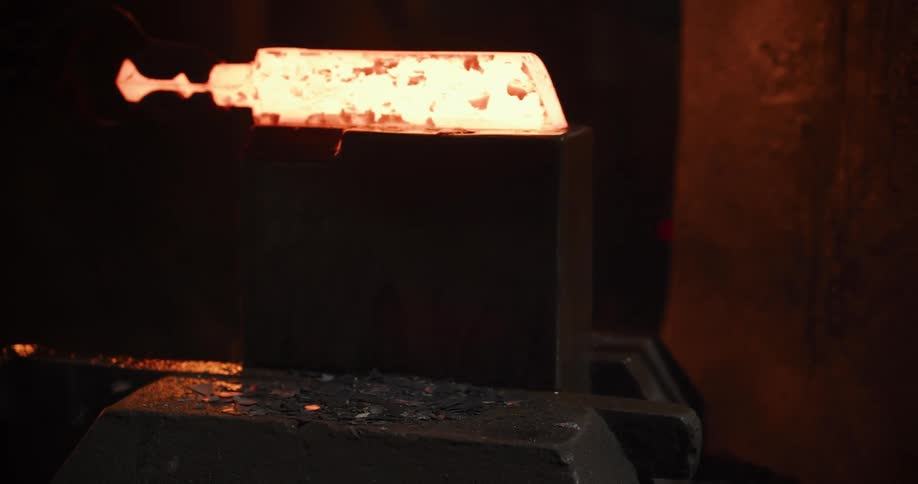 A powerful industrial press forges a glowing hot billet of metal in a dark workshop, sending sparks and flames flying with each impact