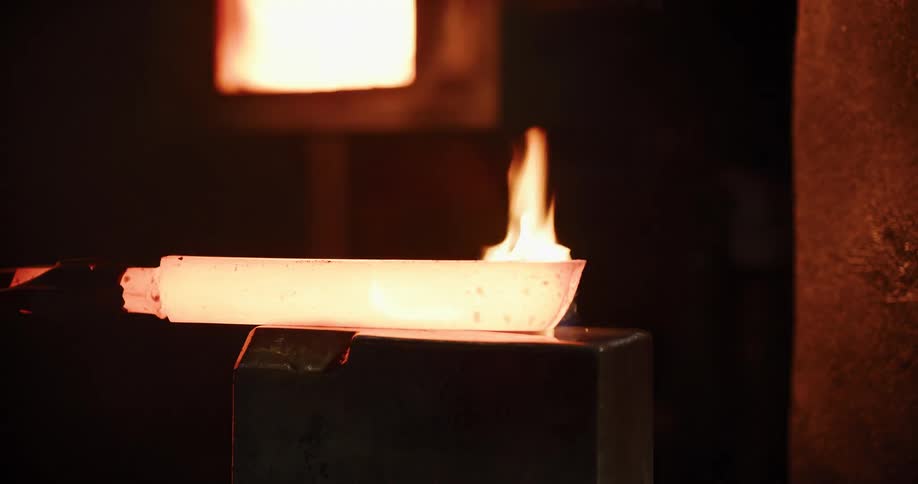 In a dark industrial workshop, a powerful automated press shapes a glowing hot piece of molten metal with fire and sparks