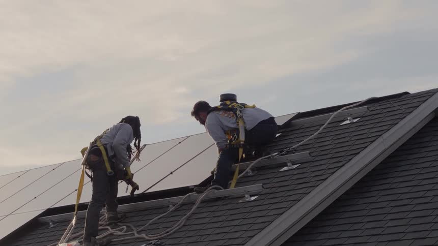 Two people are installing solar panels on a roof