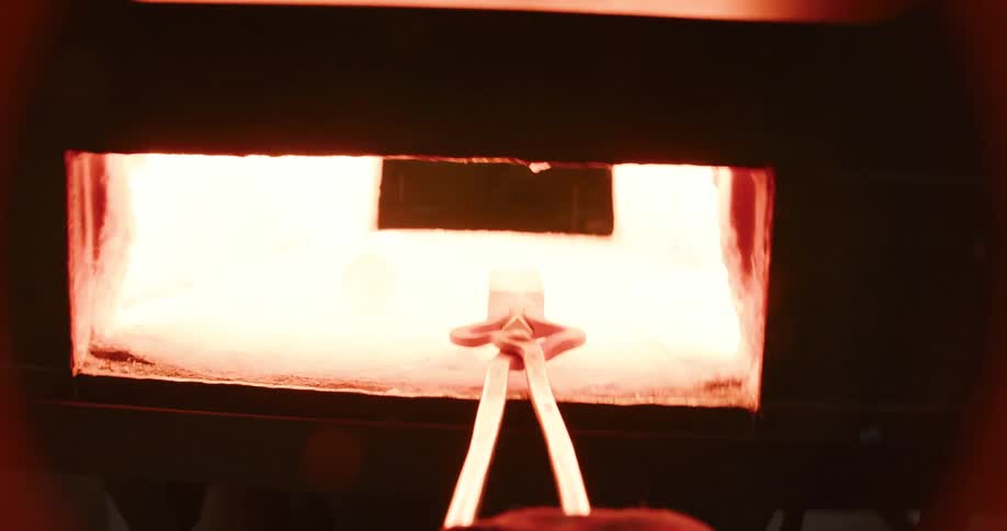 From a first-person perspective, a blacksmith carefully places a glowing piece of metal into a forge to be heated