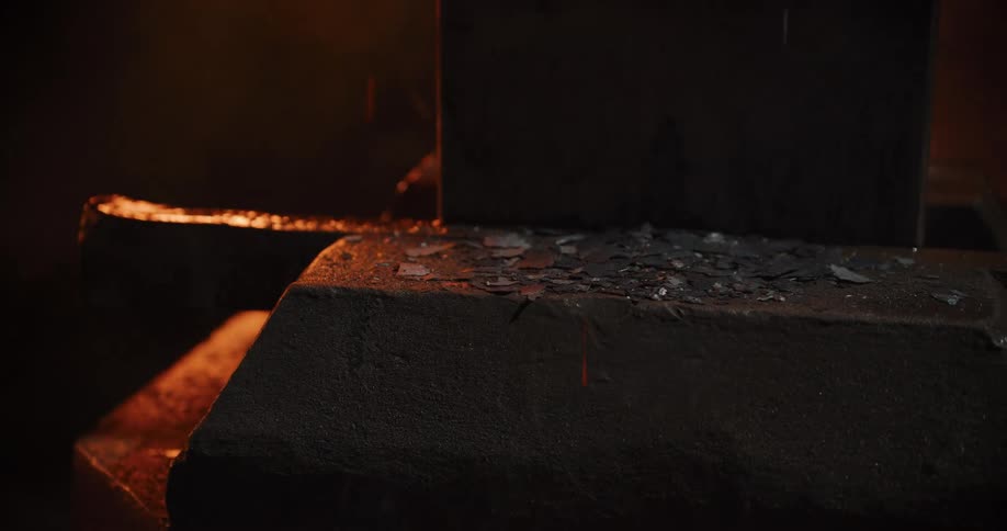 Fiery sparks and hot scale fly off an anvil as a blacksmith repeatedly strikes a glowing metal workpiece in a dark forge