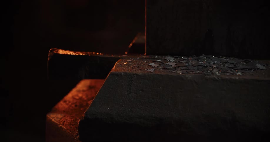 Close-up of a powerful industrial saw blade cutting through a hot metal billet in a dark workshop, showering sparks