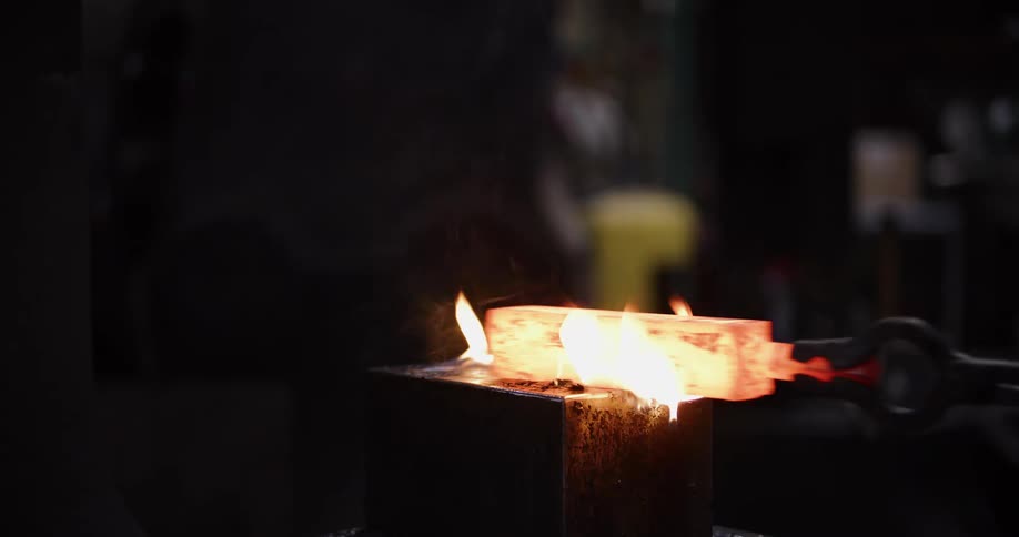 A skilled blacksmith hammers a glowing billet of steel with a large industrial press, creating sparks and flames in slow motion