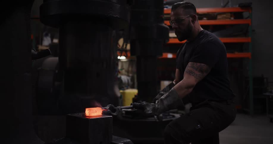 A muscular blacksmith with protective gear carefully handles a piece of red-hot, smoking metal with tongs on an anvil in his dark workshop