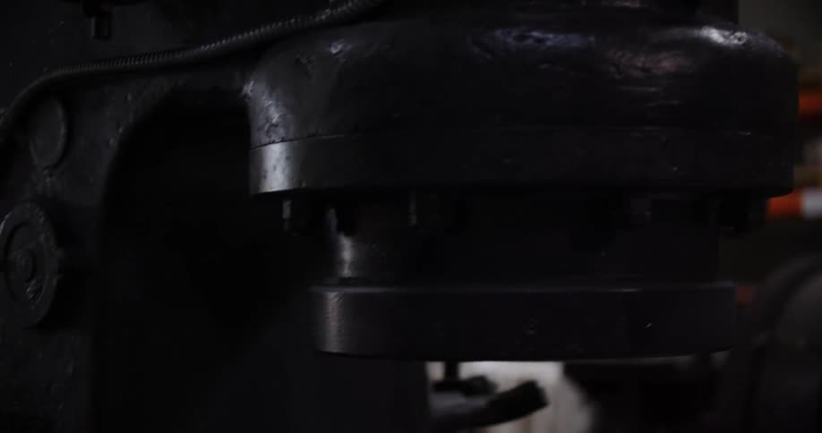 A worker wearing heavy gloves presses a button to turn on a massive industrial power hammer in a workshop