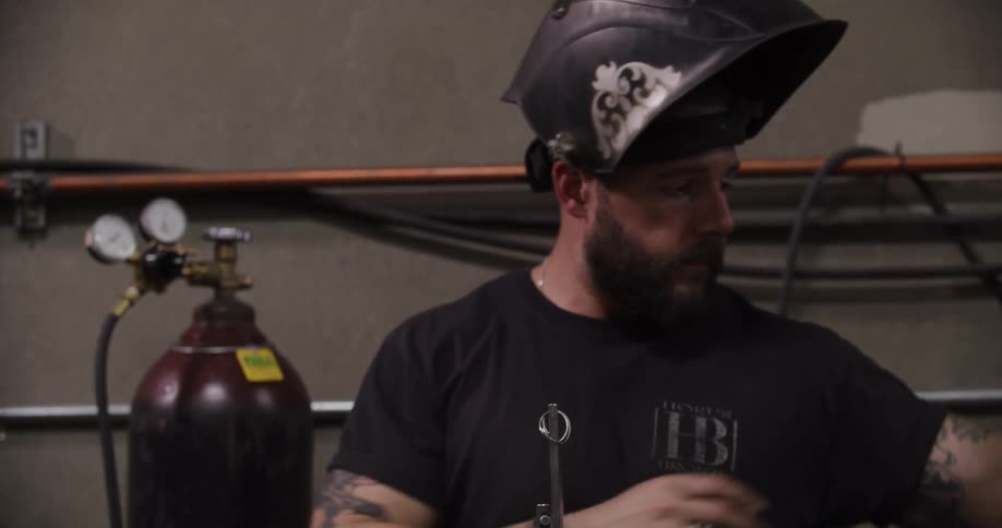 A tough-looking welder with tattoos puts on his helmet in slow motion before starting work in his workshop