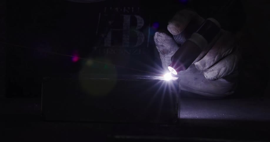 Dramatic close-up of a gloved hand guiding a welding torch, creating a brilliant flare while joining metal