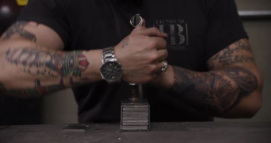 A tattooed craftsman meticulously assembles and adjusts a metal clamping tool on a magnetic base in his workshop