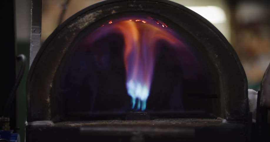A close-up shot of a powerful blue and orange gas flame burning inside a dark furnace