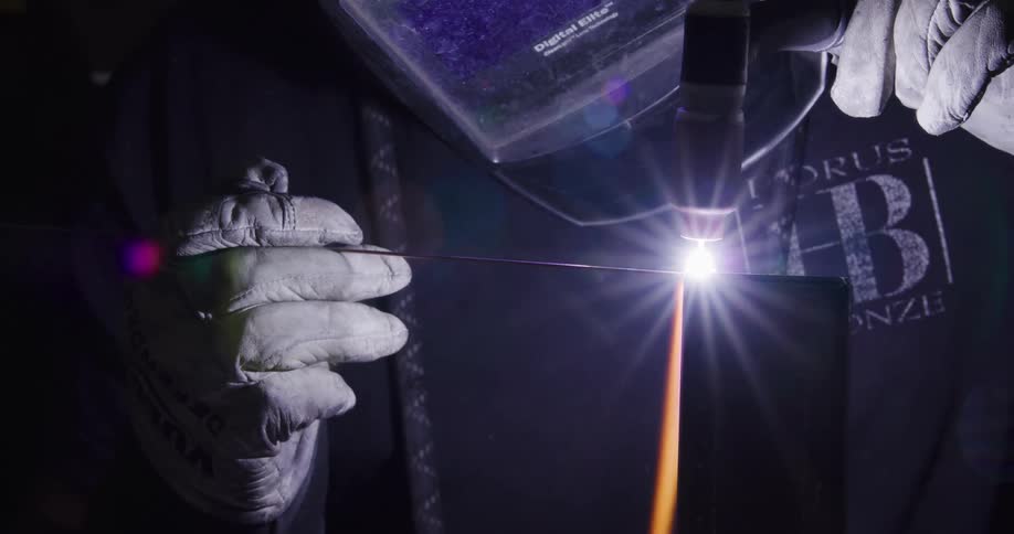 A close-up shot captures a skilled welder in a dark workshop, their torch creating a brilliant burst of light and sparks as they join metal pieces
