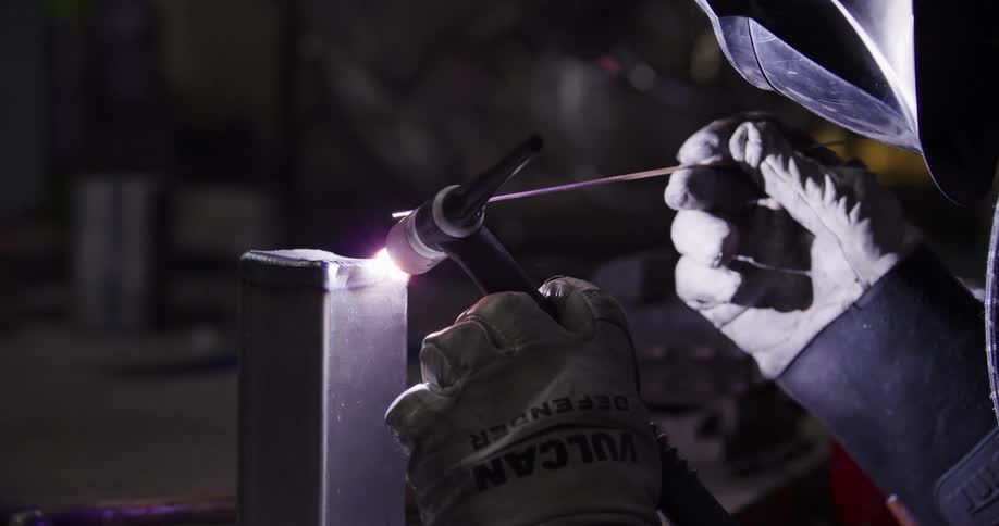 Close-up of a professional welder's hands in protective gloves expertly TIG welding a metal joint in a dimly lit workshop