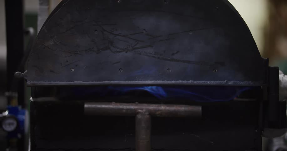 Close up of a blue flame burning inside an industrial metal forge