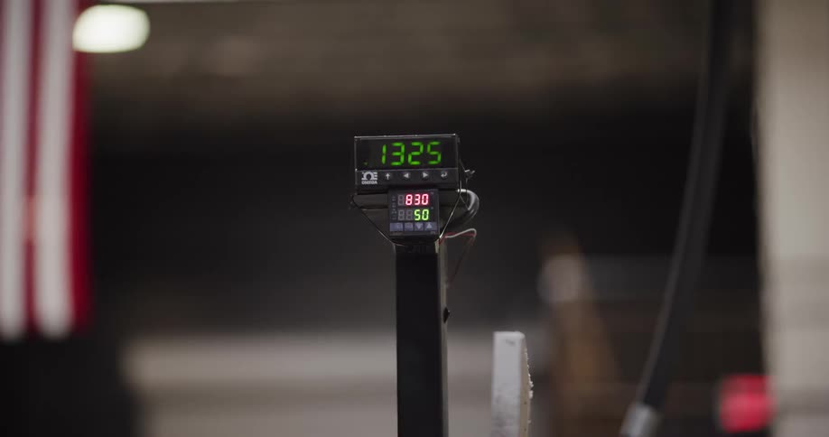 An industrial digital timer with green and red LED numbers counts up in a workshop setting