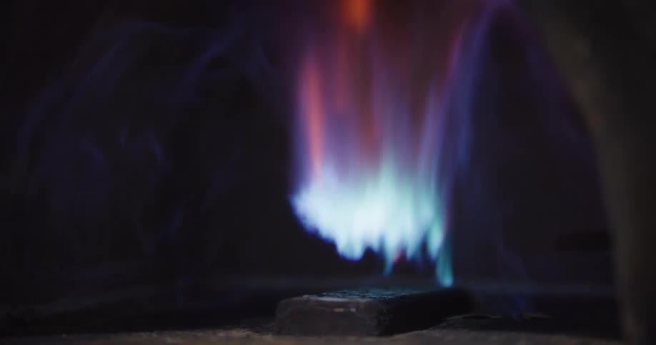 Slow motion macro shot of a gas pilot light flame dancing inside a dark furnace