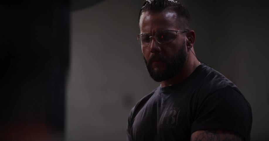 A muscular blacksmith with tattoos carefully forges a glowing hot piece of metal using a powerful industrial press in his workshop, shown in dramatic slow motion