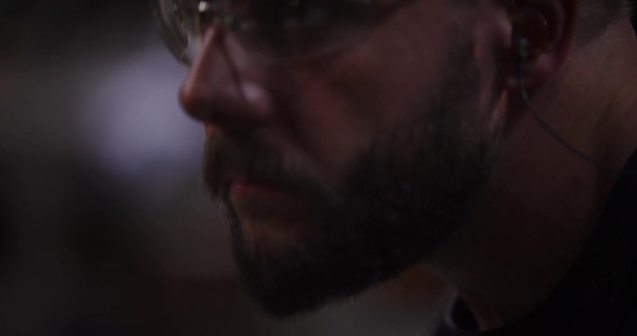 Cinematic slow-motion close-up of a focused male worker wearing safety glasses and earplugs in a dimly lit workshop