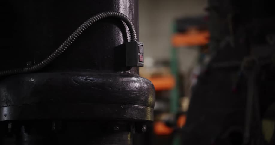 A factory worker wearing a safety glove and glasses activates a large industrial machine by pressing a button