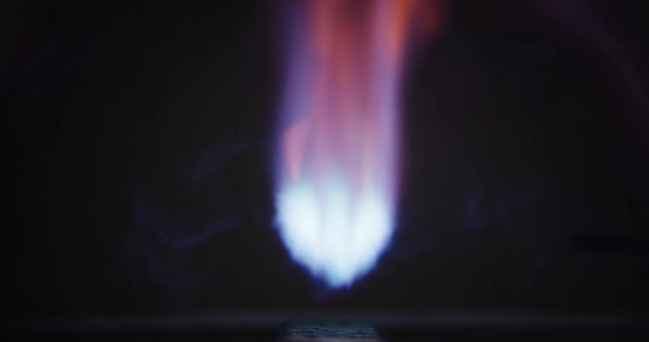 Extreme close-up in slow motion of a blowtorch heating a metal block, with vibrant blue and orange flames against a dark background