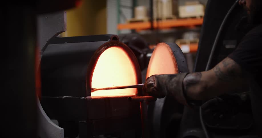 A male blacksmith places a piece of metal into a hot furnace to heat it before forging