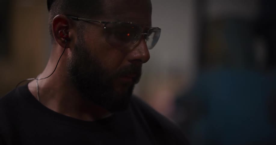 Close-up of a focused worker wearing safety glasses and earplugs in a dimly lit workshop