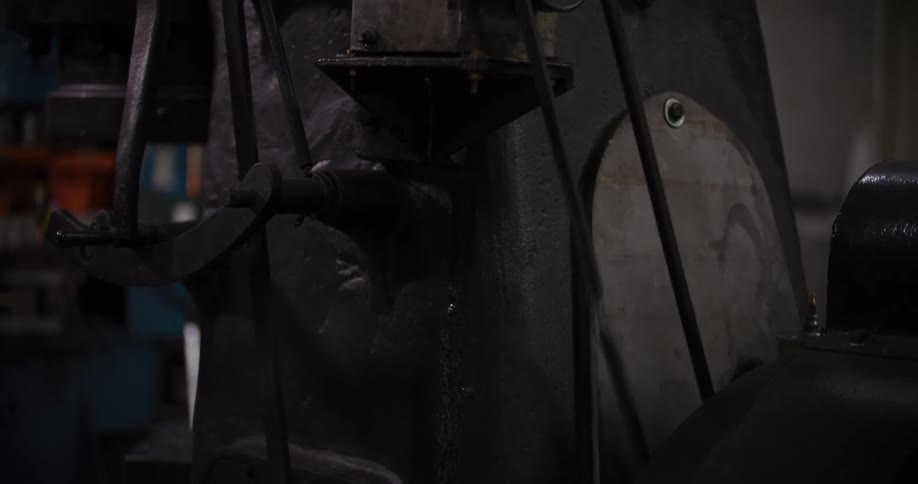 A slow tilt down on a large, black, vintage industrial machine with moving belts and wheels in a workshop