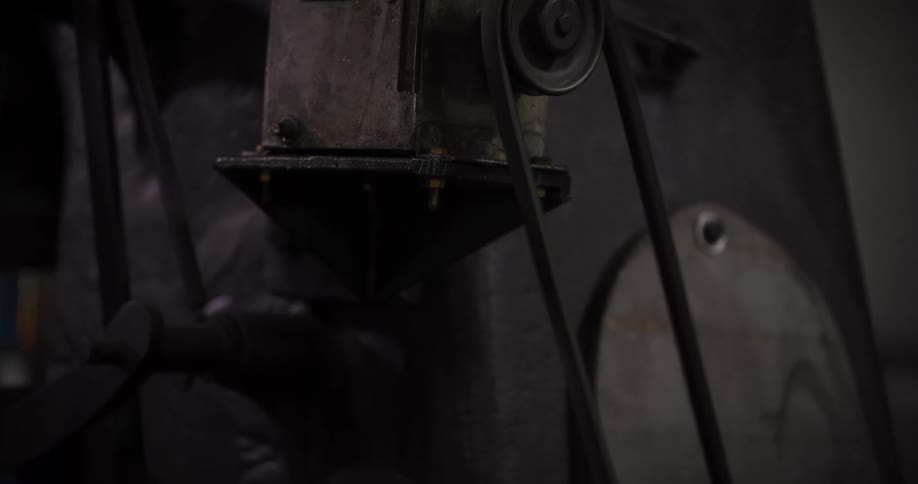 A close-up view shows the pulley and belt of an old, dark industrial machine as it powers on and begins to operate