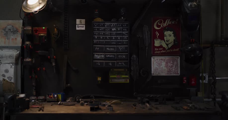 A slow zoom-out reveals a cluttered workbench and tool wall in a dimly lit industrial workshop