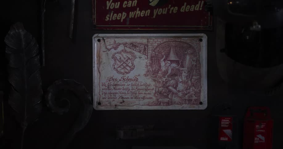 A slow focus pull reveals a vintage German sign for 'Der Schmid' (The Blacksmith) hanging on a dark, rustic wall