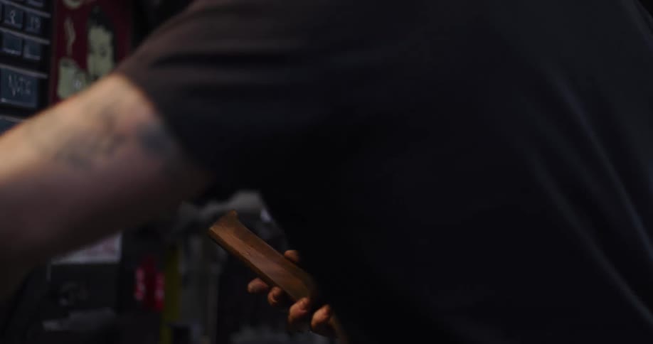 A craftsman with tattoos uses a blowtorch to char a piece of wood in his workshop before polishing it